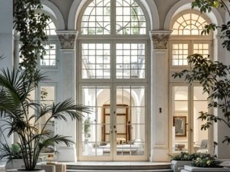 Ampia hall con finestre ad arco ed eleganti infissi, caratterizzata da piante rigogliose, decorazioni bianche, pavimenti lucidati e vista su un cortile interno. Scopri perché Roma Est offre le migliori viste della città.