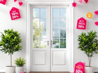 Porte doppie bianche con pannelli di vetro, fiancheggiate da piante in vaso. Cartelli rossi di vendita con sconti appesi sopra e intorno alle porte.